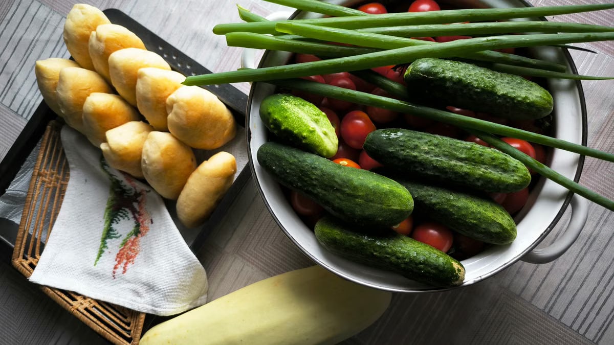 Fresh cucumbers, tomatoes, and homemade buns artfully arranged on a table for a rustic dining experience.